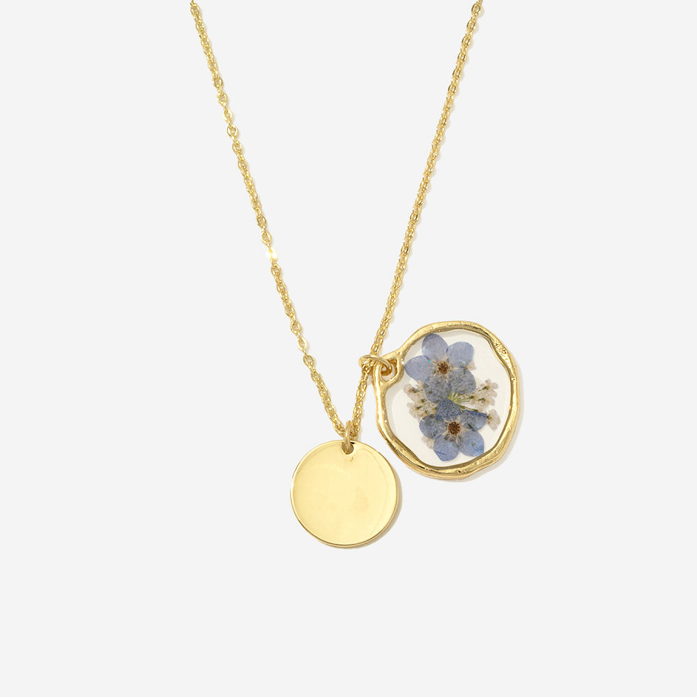 silver forget me not necklace hanging in front of blue paper