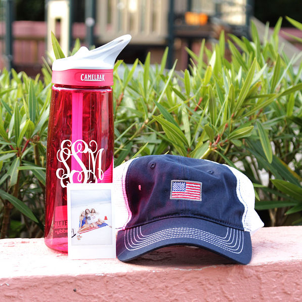 monogrammed pink camelbak with baseball hat in front of grass