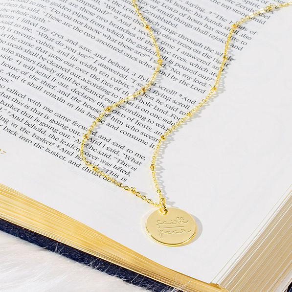 gold faith or fear necklace on book