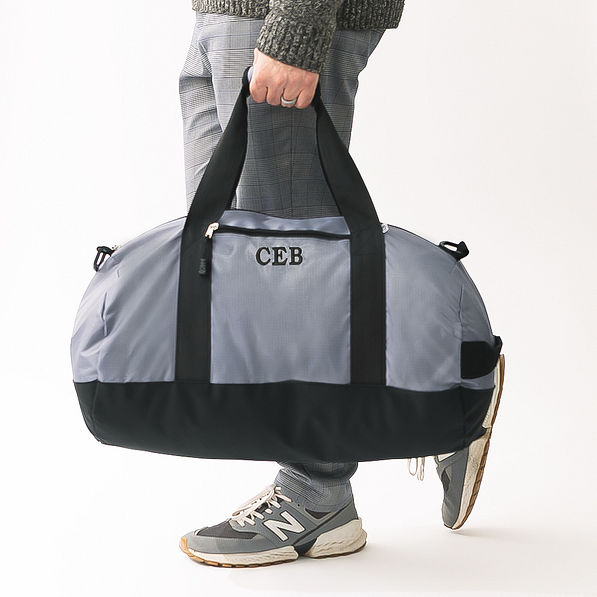 man carrying charcoal and black monogrammed packable travel bag