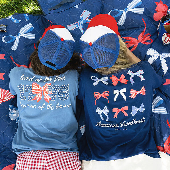 women laying on picnic blanket wearing light navy and bows america t shirt