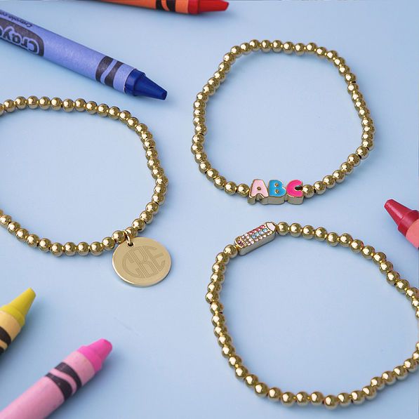 Gold monogrammed beaded teacher bracelets stack on blue with crayons