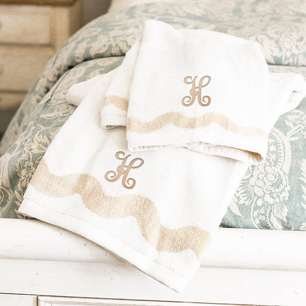bath towel set on bed with tan interlocking inital