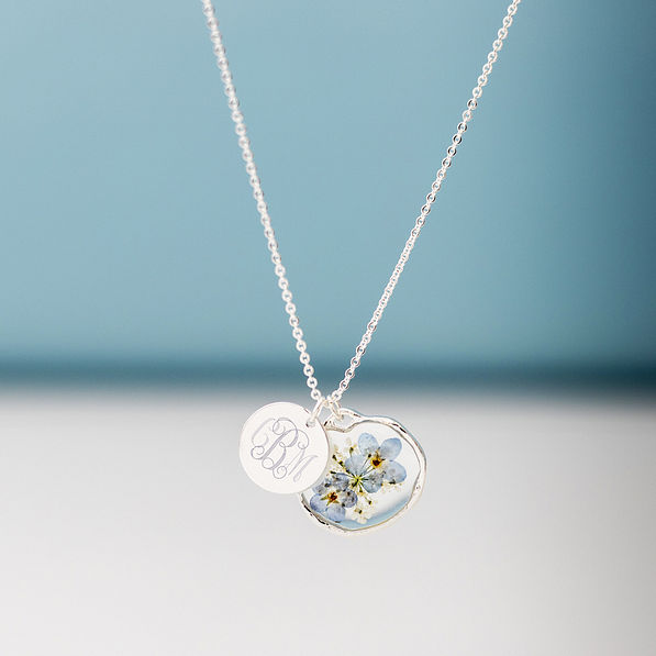 silver forget me not necklace hanging in front of blue paper
