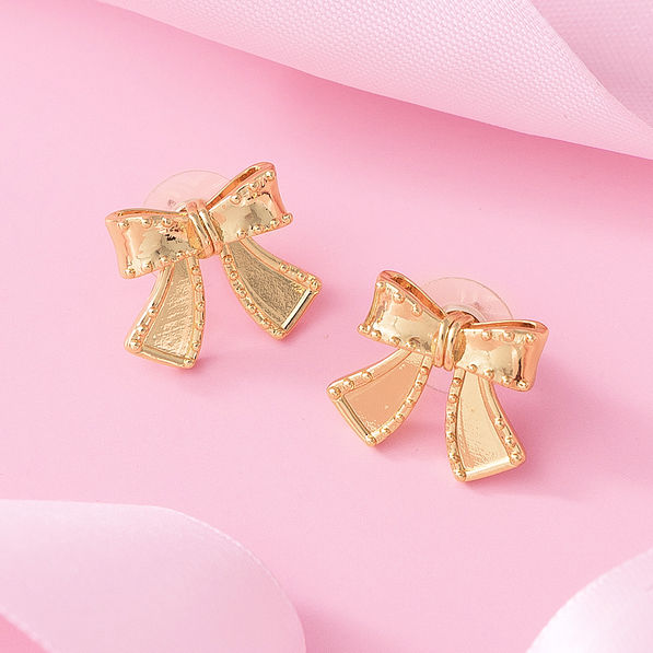 gold bow stud earrings on pink background