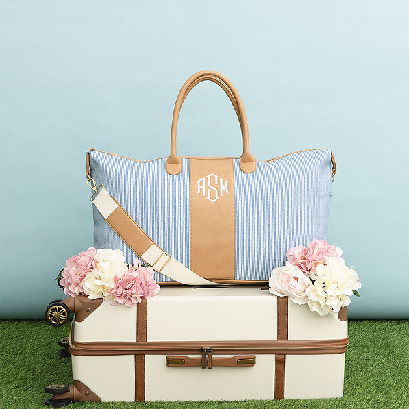 navy seersucker weekender and vintage suitcase on grass and blue