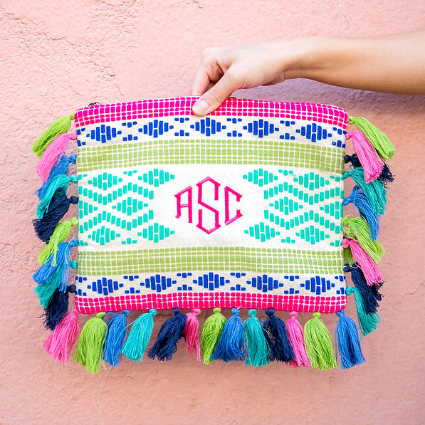 bright monogrammed clutch with tassels on edges in front of pink wall