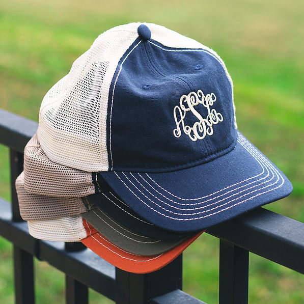 monogrammed snapback baseball hats stacked on fence with grass in background