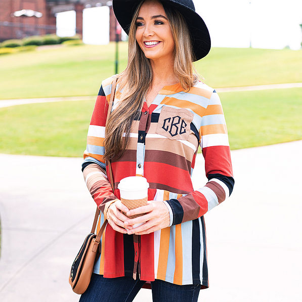 woman wearing monogrammed striped peplum top with black floppy hat and holding coffee