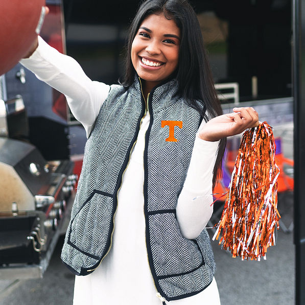 girl wearing tennessee herringbone vest and holding football and pom pom