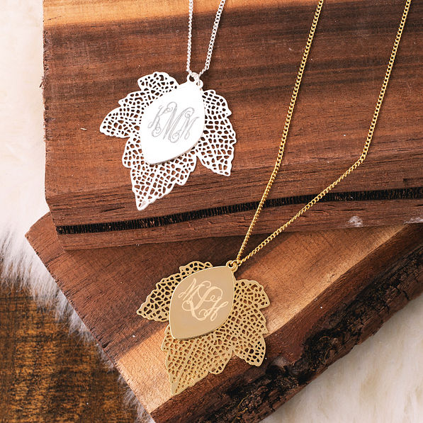 silver and gold monogrammed leaf necklaces on wood