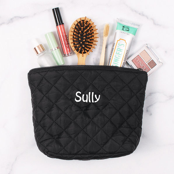 toiletries spilling out of black quilted cosmetic case with name