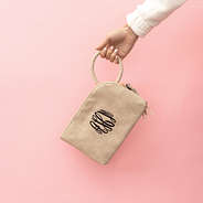 taupe monogrammed wristlet clutch in front of pink paper