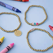 Gold monogrammed beaded teacher bracelets stack on blue with crayons