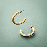 gold brush hoop earrings on green background