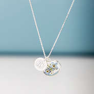 silver forget me not necklace hanging in front of blue paper