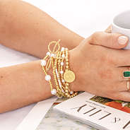 monogrammed pearl bow bracelet stack in gold on wrist with coffee