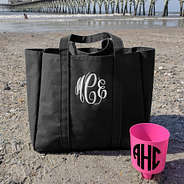 black monogrammed essential tote sitting in sand on beach