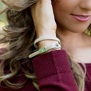 tan monogrammed wrap bracelet on wrist with burgundy sweater