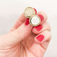 gold monogrammed circle earrings being held with pink nails