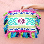 bright monogrammed clutch with tassels on edges in front of pink wall
