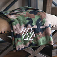 folded monogrammed fleece blanket in camo laying on bench