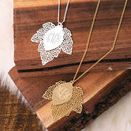 silver and gold monogrammed leaf necklaces on wood