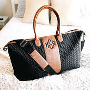 monogrammed black and brown quilted travel bag on bed