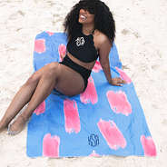 girl sitting on blue and pink paintbrush towel at beach