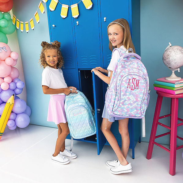 2 girls holding blue quilted backpack and mermaid backpack