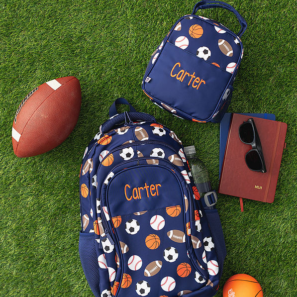sports ball backpack and lunchbox flatlay on grass