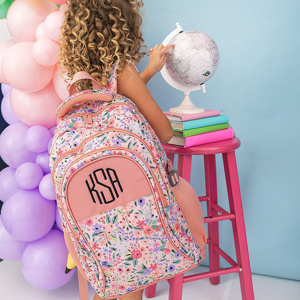 girl looking at globe with monogrammed coral floral backpack