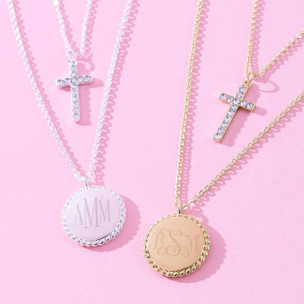 close up of monogrammed kids cross necklace in gold and silver on pink paper