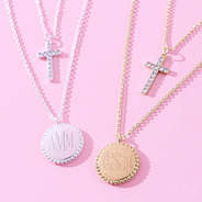 close up of monogrammed kids cross necklace in gold and silver on pink paper